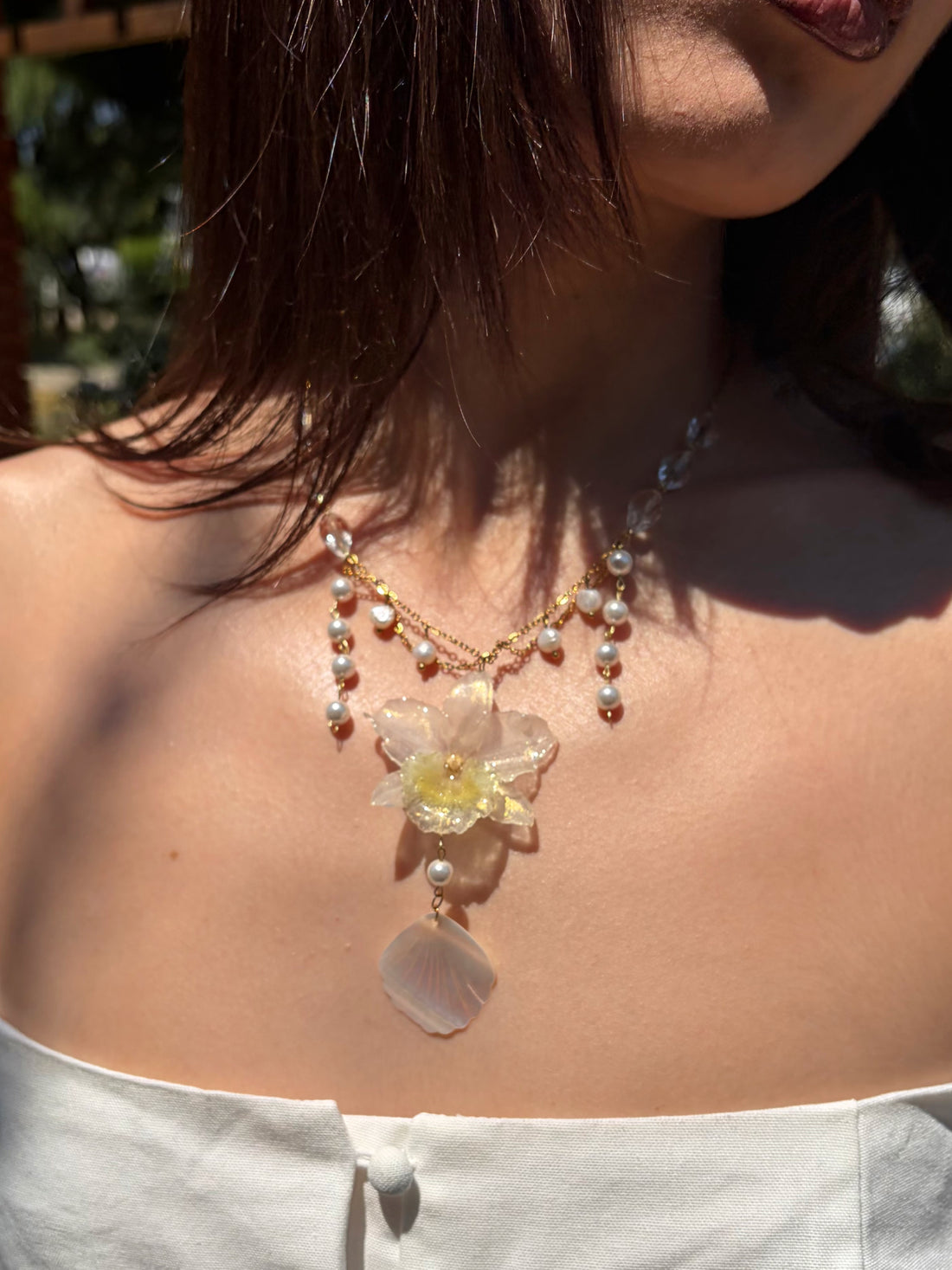 Necklace with a floral pendant and pearl details worn by a person outdoors.