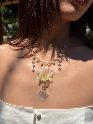 Necklace with a floral pendant and pearl details worn by a person outdoors.
