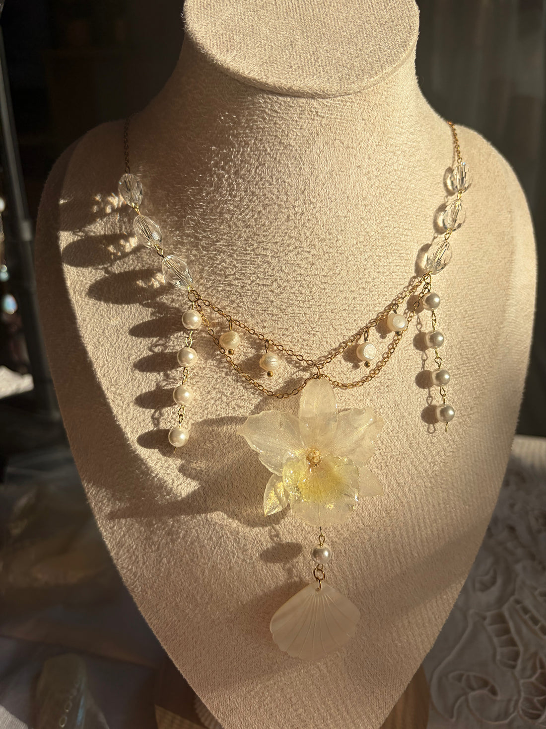 Necklace with a floral pendant and pearl details worn by a person outdoors.