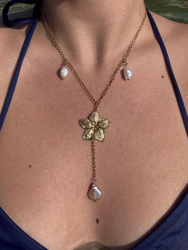 Necklace with a floral pendant and pearl drops worn by a person against a natural background.